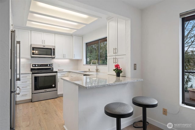 kitchen featuring a breakfast bar, a peninsula, a sink, white cabinets, and appliances with stainless steel finishes