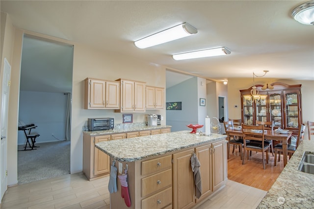 kitchen with light brown cabinets, lofted ceiling, light hardwood / wood-style flooring, a kitchen island, and light stone counters