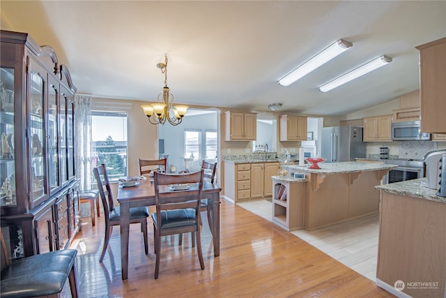 dining room with light hardwood / wood-style floors, vaulted ceiling, sink, and an inviting chandelier