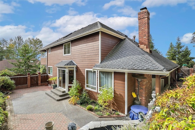 rear view of house with entry steps, a shingled roof, a chimney, fence, and a patio area