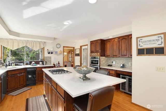 kitchen with beverage cooler, a kitchen island, stainless steel appliances, light countertops, and a sink