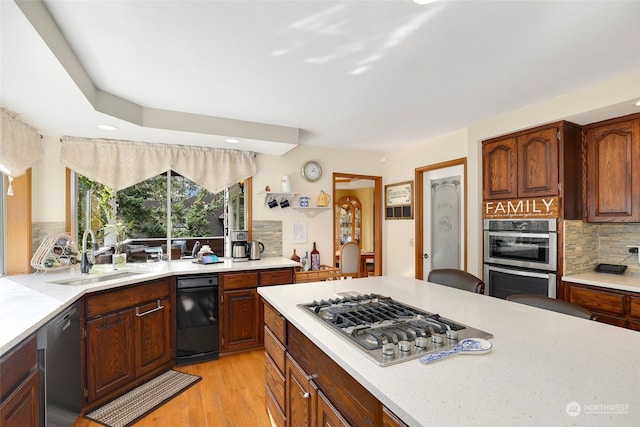 kitchen with a sink, light wood-style floors, light countertops, appliances with stainless steel finishes, and backsplash