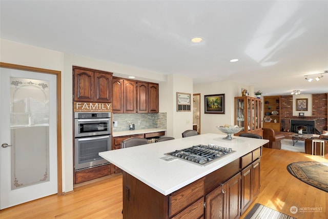 kitchen featuring a kitchen island, light wood-style floors, light countertops, appliances with stainless steel finishes, and backsplash