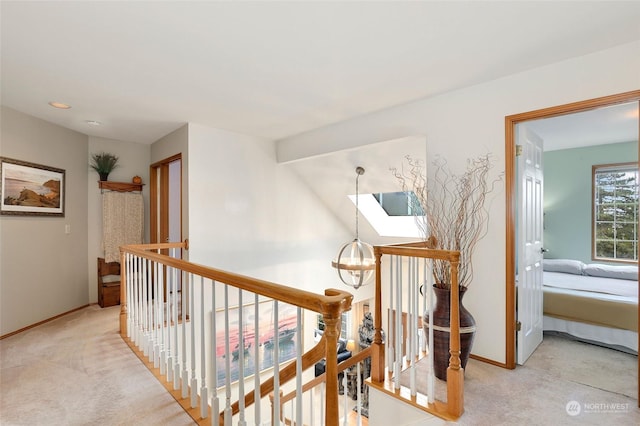 corridor featuring baseboards, a notable chandelier, an upstairs landing, and light colored carpet