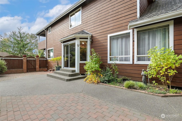 rear view of house with entry steps, fence, roof with shingles, a gate, and a patio area