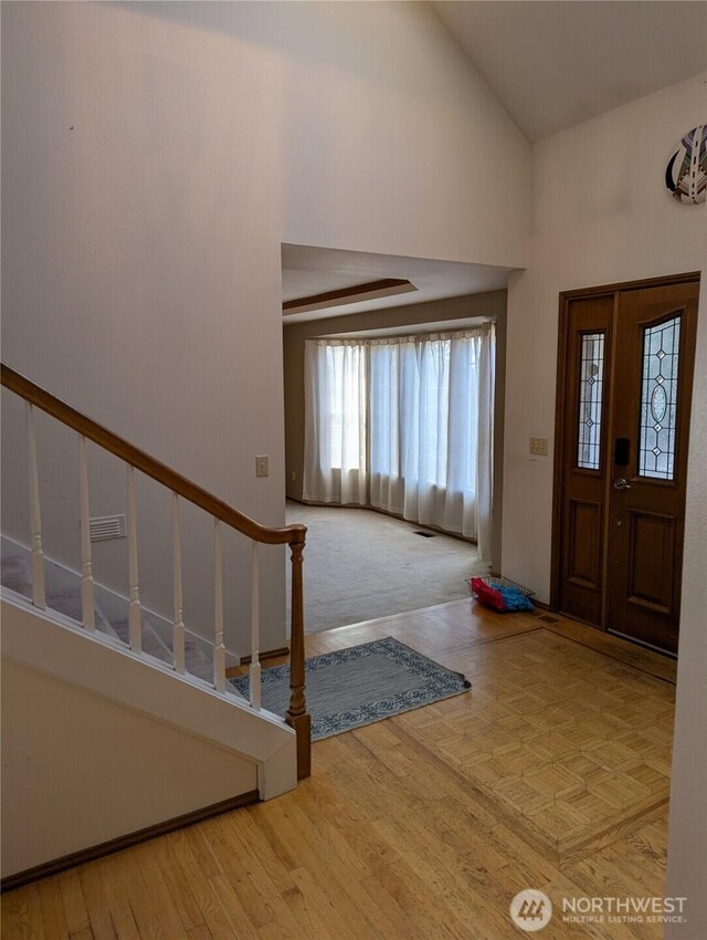 foyer entrance featuring high vaulted ceiling, visible vents, stairway, and wood finished floors