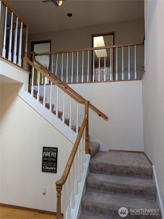 staircase featuring baseboards and a high ceiling