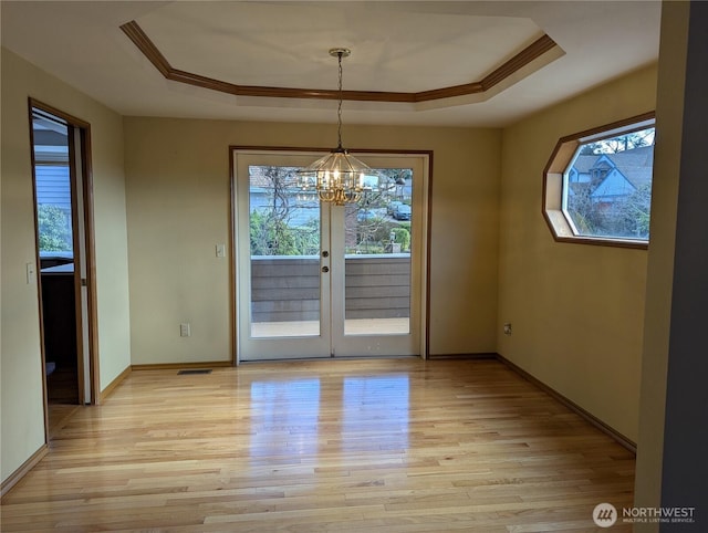 unfurnished dining area featuring light wood-type flooring, a tray ceiling, a notable chandelier, and baseboards