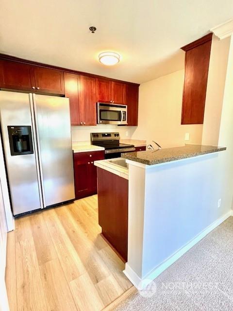 kitchen with dark stone counters, kitchen peninsula, stainless steel appliances, and light wood-type flooring