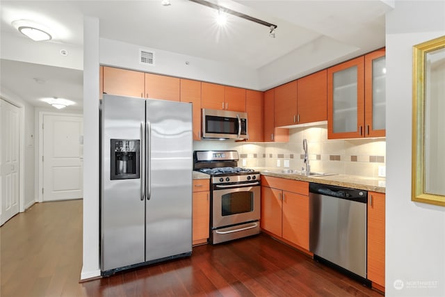 kitchen with dark hardwood / wood-style floors, tasteful backsplash, stainless steel appliances, light stone counters, and sink