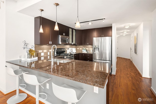 kitchen featuring kitchen peninsula, appliances with stainless steel finishes, dark brown cabinets, and hanging light fixtures