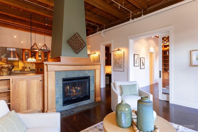 living room featuring beam ceiling, a tiled fireplace, dark wood-type flooring, and wood ceiling