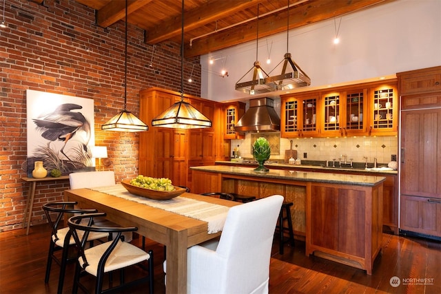 bar with beamed ceiling, wall chimney exhaust hood, hanging light fixtures, and a high ceiling