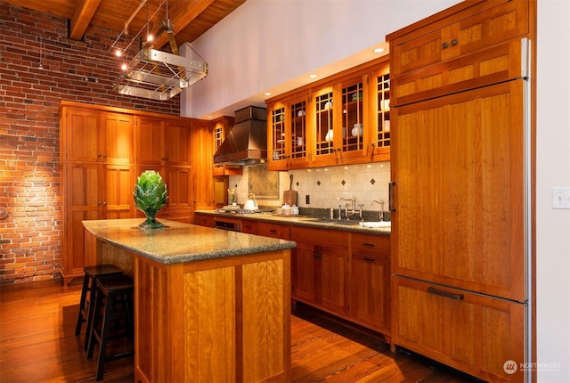 kitchen with a high ceiling, beamed ceiling, wood-type flooring, a kitchen island, and custom range hood