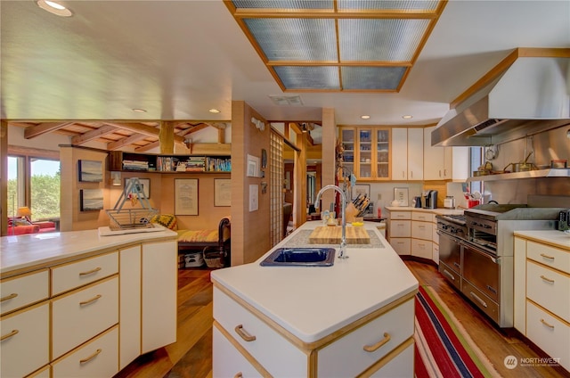 kitchen with dark wood-type flooring, wall chimney range hood, high end stainless steel range oven, ventilation hood, and a kitchen island with sink