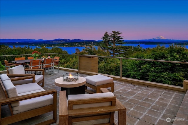 patio terrace at dusk featuring a water and mountain view and an outdoor fire pit