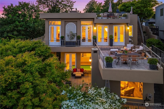 back house at dusk with an outdoor living space, a patio, and french doors