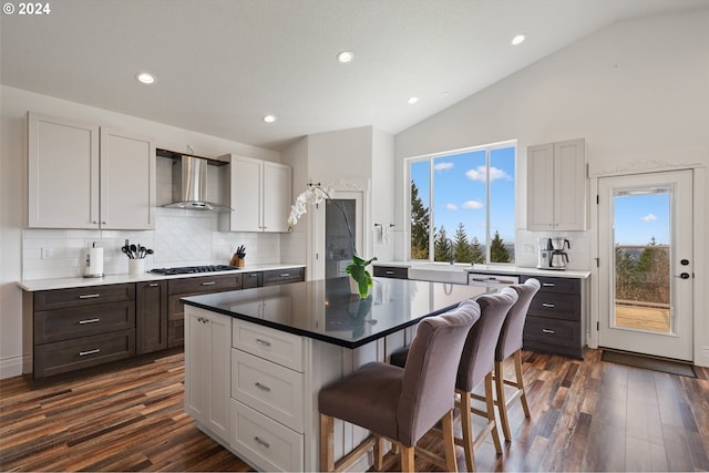 kitchen featuring a breakfast bar, stainless steel gas stovetop, lofted ceiling, a center island, and wall chimney exhaust hood