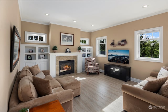 living room featuring built in features, a fireplace, light hardwood / wood-style flooring, and ornamental molding