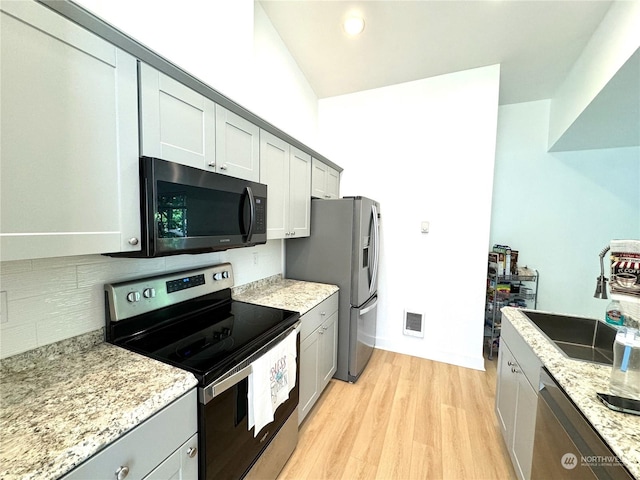 kitchen featuring light stone counters, gray cabinets, stainless steel appliances, and light wood-type flooring