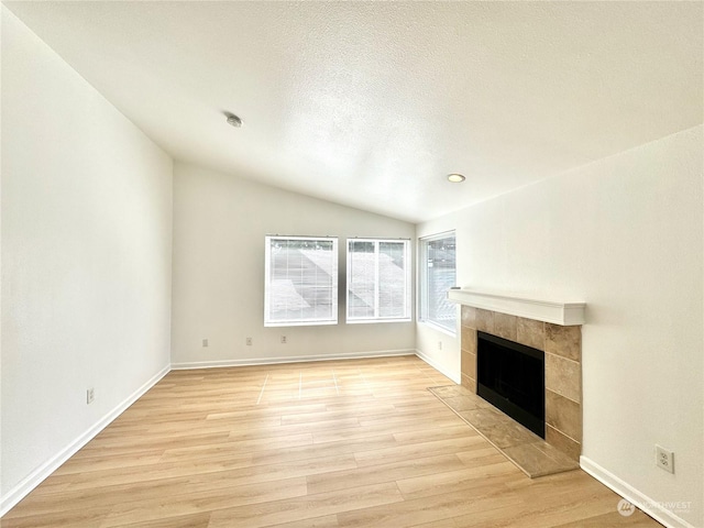 unfurnished living room with lofted ceiling, a fireplace, light hardwood / wood-style floors, and a textured ceiling