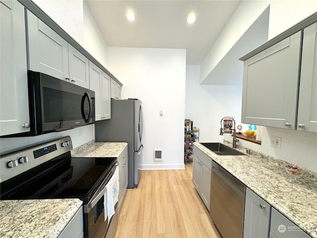 kitchen with sink, light hardwood / wood-style flooring, appliances with stainless steel finishes, gray cabinetry, and light stone counters