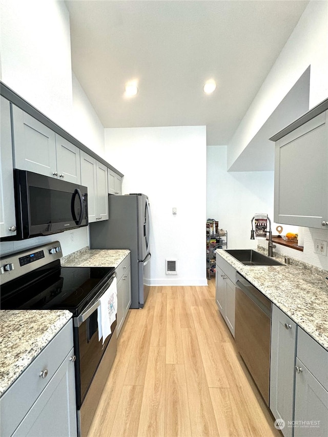 kitchen with sink, gray cabinetry, light stone counters, appliances with stainless steel finishes, and light hardwood / wood-style floors