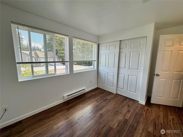 unfurnished bedroom featuring a baseboard heating unit, dark hardwood / wood-style floors, and a closet