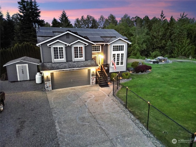 bi-level home with a lawn, solar panels, a storage unit, and a garage