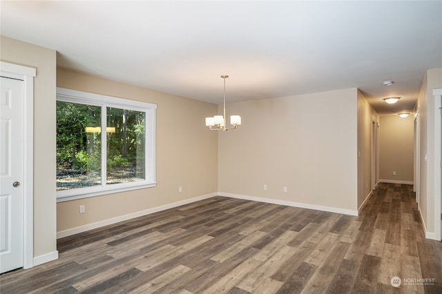 empty room with a notable chandelier and dark wood-type flooring