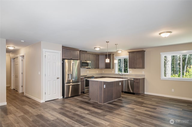 kitchen with appliances with stainless steel finishes, a center island, dark hardwood / wood-style floors, and pendant lighting