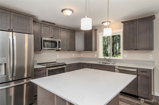 kitchen featuring decorative light fixtures, dark hardwood / wood-style flooring, a kitchen island, sink, and appliances with stainless steel finishes