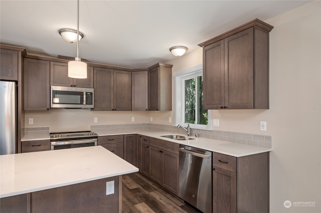 kitchen with light stone counters, dark hardwood / wood-style flooring, hanging light fixtures, appliances with stainless steel finishes, and sink