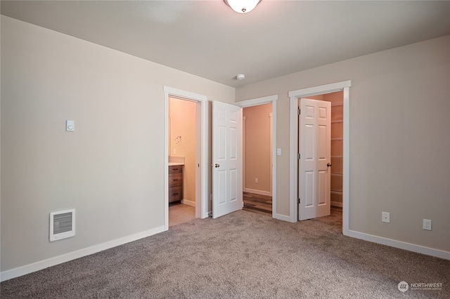 unfurnished bedroom with a spacious closet, connected bathroom, and carpet flooring