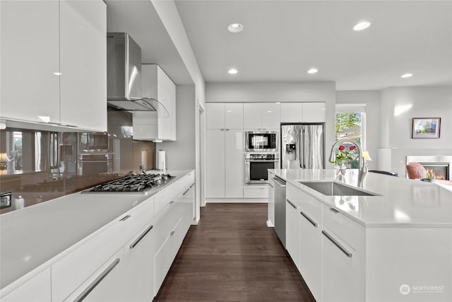 kitchen with stainless steel appliances, dark wood-type flooring, wall chimney range hood, sink, and white cabinets