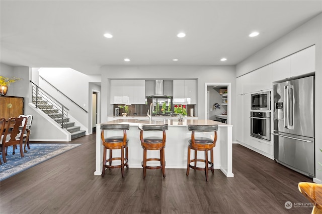 kitchen featuring a kitchen breakfast bar, white cabinets, wall chimney range hood, and appliances with stainless steel finishes