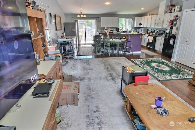 interior space featuring vaulted ceiling, black appliances, white cabinets, a chandelier, and a kitchen island