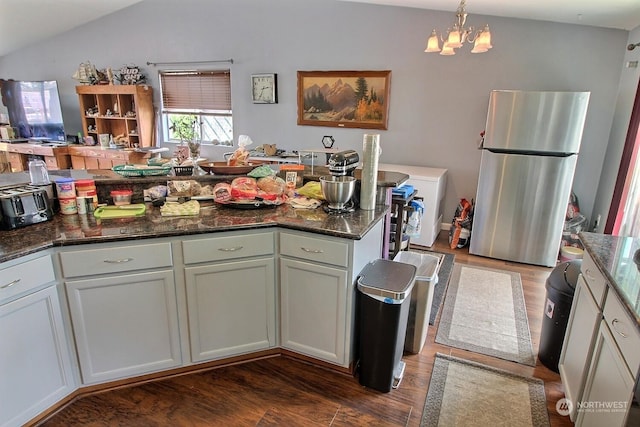 kitchen with stainless steel fridge, dark hardwood / wood-style flooring, dark stone countertops, a chandelier, and hanging light fixtures