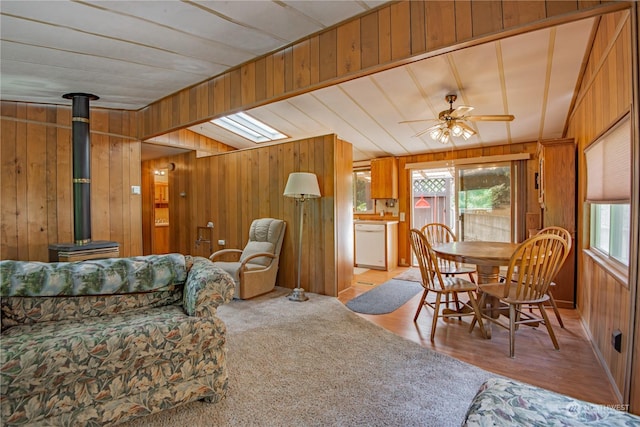 carpeted living room featuring a wood stove, ceiling fan, and wood walls