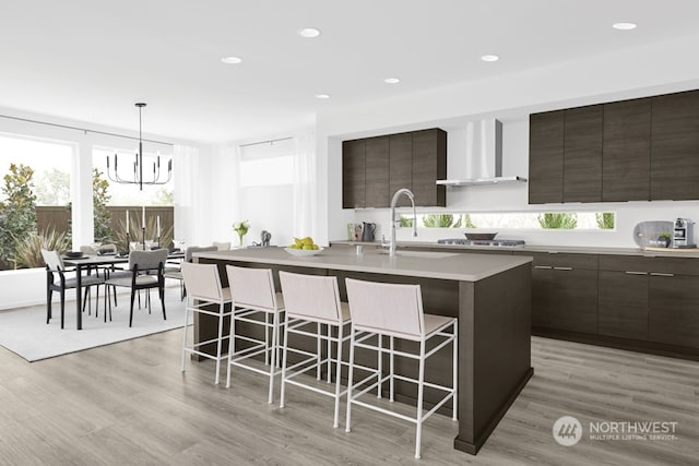 kitchen with a kitchen island with sink, stainless steel gas stovetop, a kitchen breakfast bar, and wall chimney exhaust hood