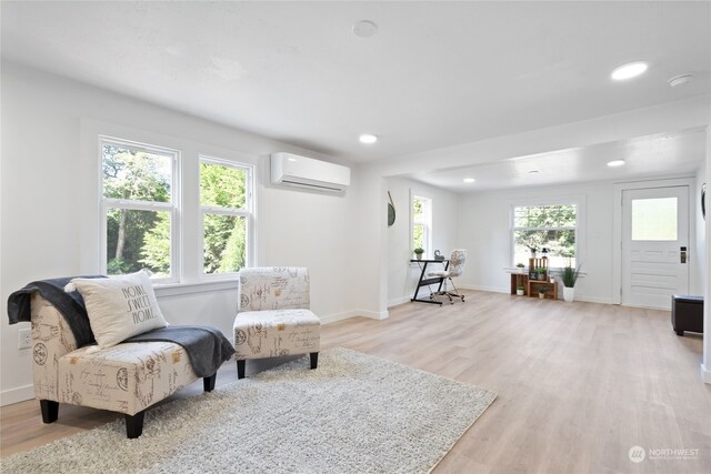 living area featuring a healthy amount of sunlight, a wall unit AC, and light hardwood / wood-style floors