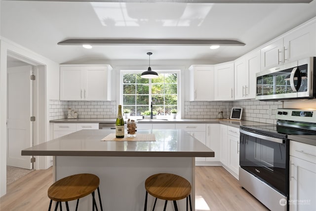 kitchen featuring hanging light fixtures, white cabinetry, appliances with stainless steel finishes, and a kitchen breakfast bar