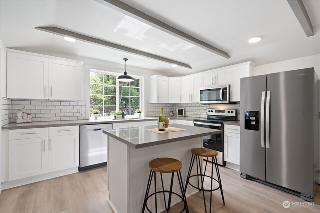 kitchen featuring white cabinetry, decorative light fixtures, a center island, appliances with stainless steel finishes, and beam ceiling