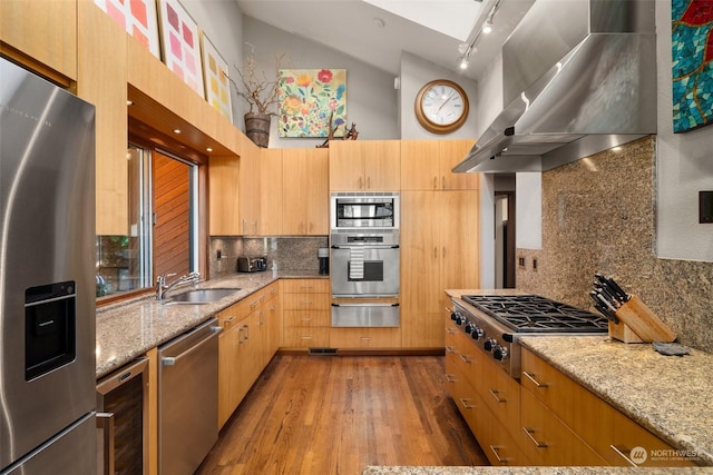 kitchen featuring light stone countertops, sink, stainless steel appliances, wall chimney range hood, and track lighting