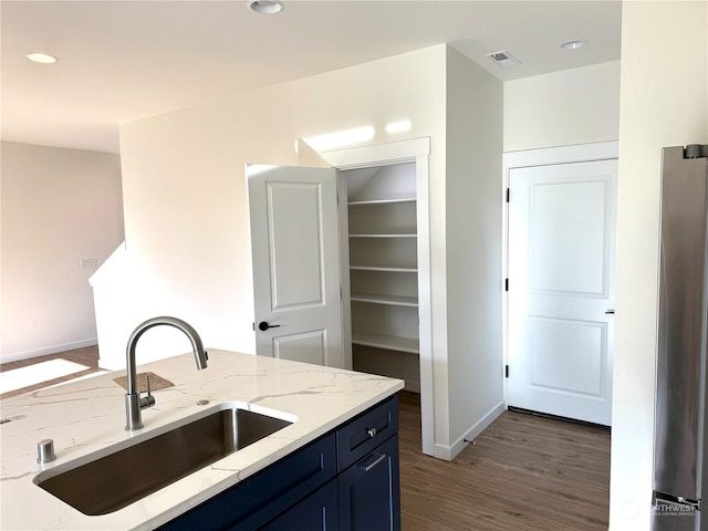 kitchen with light stone countertops, blue cabinetry, dark wood-type flooring, and sink