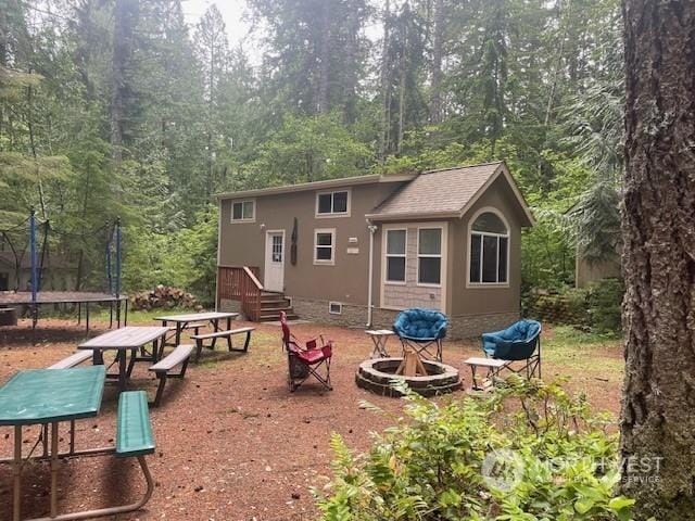 rear view of property with a fire pit and a trampoline