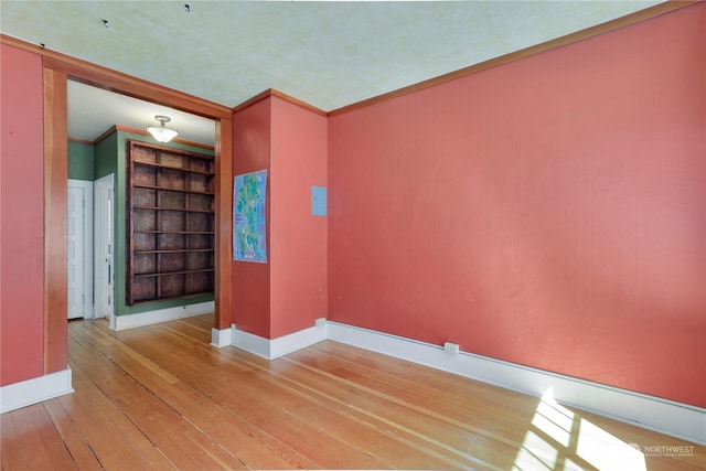 unfurnished room featuring built in shelves, light wood-type flooring, and crown molding