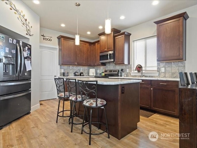 kitchen with hanging light fixtures, a breakfast bar, light hardwood / wood-style flooring, a kitchen island, and appliances with stainless steel finishes