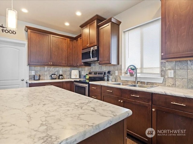 kitchen featuring stainless steel appliances, decorative light fixtures, light stone countertops, sink, and tasteful backsplash