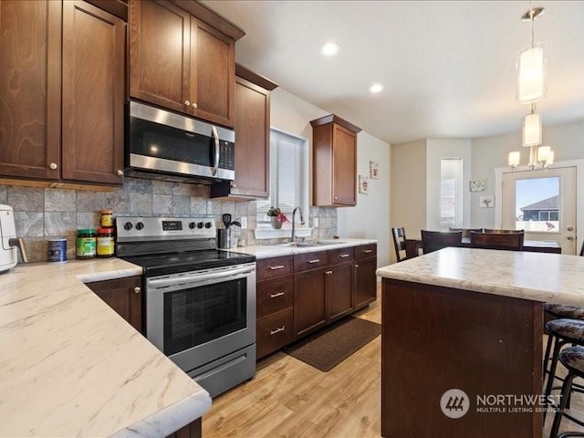 kitchen with appliances with stainless steel finishes, light hardwood / wood-style flooring, tasteful backsplash, a breakfast bar area, and decorative light fixtures